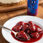 Strawberries in aged balsamic syrup with cracked black pepper, cheesecake in the background